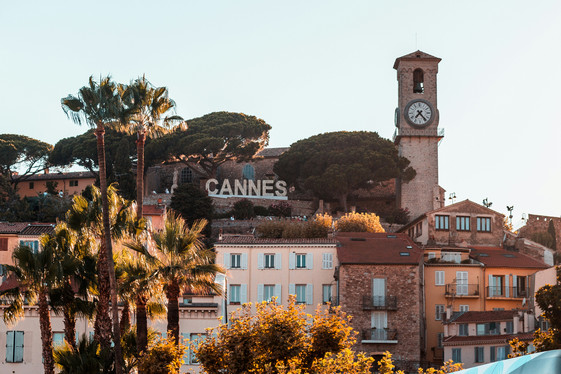 Vue de Cannes au soleil couchant avec palmiers et enseigne de la ville